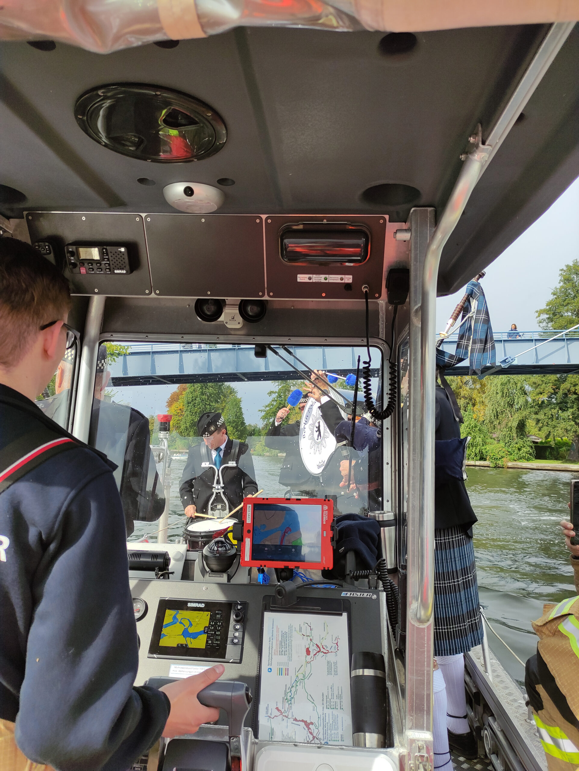 Blick durch den Führerstand eines Feuerwehr-Merzweckbootes auf die davor auf dem Boot stehende Berlin Police Pipe Band